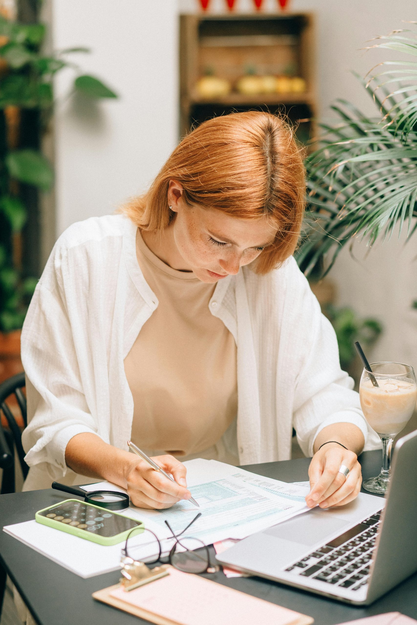 Woman analyzing financial documents using laptop and calculator indoors.